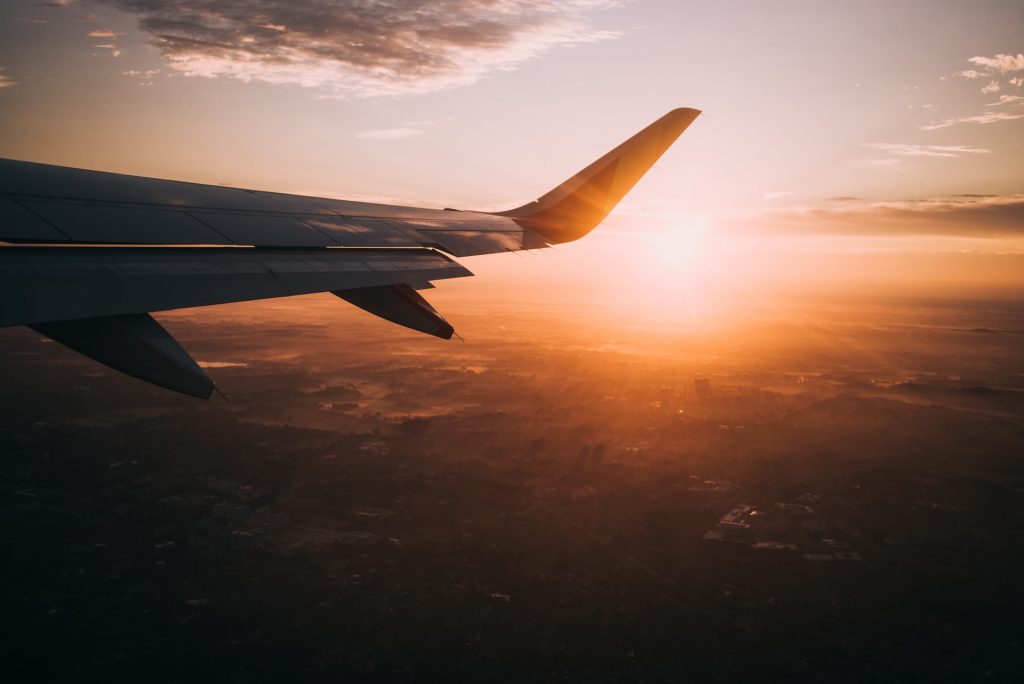 foto da asa de um avião em pleno voo com o por do sol ao fundo